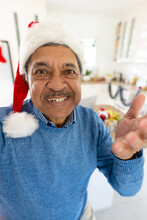 Vertical Image Of Smiling Senior Biracial Man In Santa Hat Making Christmas Video Call At Home