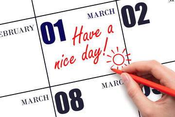 The hand writing the text Have a nice day and drawing the sun on the calendar date March 1