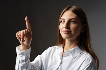 Young female entrepreneur touching virtual screen against grey studio background