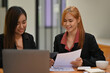 © saltdium - Two of Asian businesswomen working with a document and laptop.
