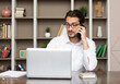 © Vitaliy - Portrait of young handsome business man working on laptop and talking to phone in the modern office