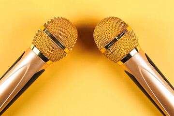 Wall Mural - Two golden microphones isolated on yellow background close up