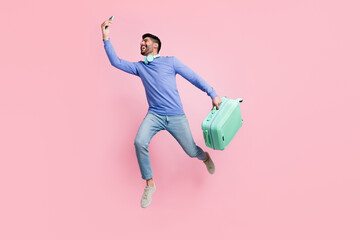 Wall Mural - Full length photo of pretty cute arab guy dressed blue pullover jumping vlogging device holding baggage isolated pink color background