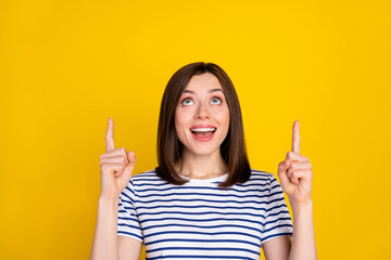 Wall Mural - Photo of young attractive cute smiling woman directing fingers up looking empty space unexpected good news isolated on yellow color background