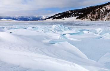 Wall Mural - Winter landscape of snow-covered frozen Baikal Lake at frosty day in January. Ice hummocks are swept up by dense snow crust. The mountains are covered with low clouds. Cold natural background