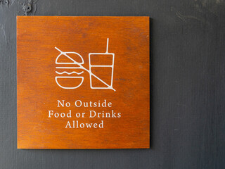 A light brown sign over a dark grey background banning people to bring in food and drinks in a local cafe.