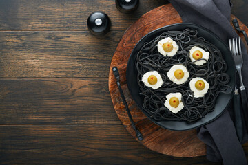 Halloween party Italian black pasta decorated horror  olives like eyes on black plate on old dark table background. Monster face from pasta. Halloween decorations and Halloween food concept. Mock up.