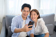 © tonefotografia - Young smiling asian couple using smartphone in living room at home