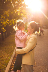 authentic portrait of mother and her daughter in autumn park during sunset. enjoying time together