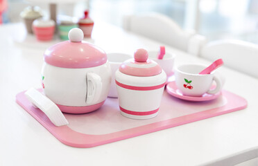 A set of pink white pastel color wood  toy tea cups including 2 coffee cups with teaspoons, a teapot, a sugar jar  and a milk jug is placed on a tray.