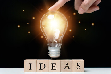 Poster - New concept concept. A glowing lamp placed on a wooden block with the word idea written on.