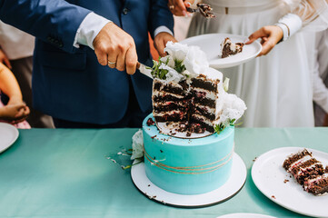 Wall Mural - The bride and groom cut the sweet, delicious wedding cake, which is on the table, into a piece with a knife at the ceremony.