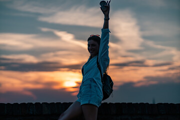 Wall Mural - a portrait of beautiful girl tourist standing leaned on a brick fence of old fortress. she is happy about visiting new place, holding paper map and cup of coffee. 