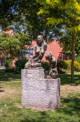 Europe, France, Dunkerque - July 9, 2022: Modern art piece featuring 2 naked sitting women in Parc de la Marine. Gray stone against green foliage and lawn. Red wall through foliage.