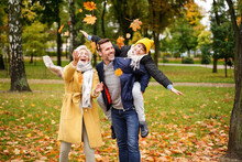 Happy Mom, Dad And Son Having Fun Together In The Autumn Park, Throwing Golden Leaves And Laughing.