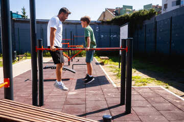 father exercising with his son on a dip station at outdoor gym