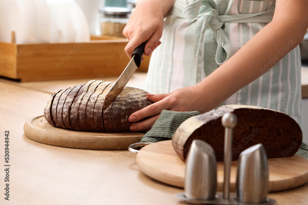 Woman cutting fresh bread on counter in kitchen, closeup