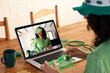 Caucasian woman holding shamrock glasses while having a video call on laptop at home