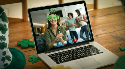 Wall Mural - Webcam view of caucasian woman wearing shamrock glasses on video call on laptop on wooden table