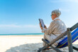 © CandyRetriever  - Modern Asian senior businesswoman working on digital tablet with internet at tropical beach in sunny day. Elderly retired woman enjoy outdoor lifestyle with using technology on summer holiday vacation