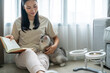 © CandyRetriever  - Young beautiful Asian woman relaxing with white tabby cat in apartment living room and reading a book. Happy girl relax and enjoy indoors lifestyle and leisure activity with pet on vacation at home.