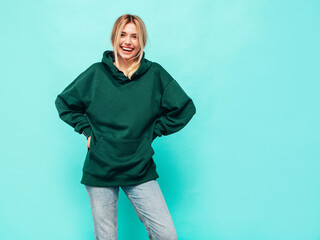 young beautiful smiling female in trendy summer green hoodie. sexy carefree woman posing near blue w