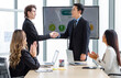 © Bangkok Click Studio - Millennial Asian successful professional male businessmen in formal suit standing shaking hands together while unrecognizable female colleagues clapping hands applaud in company office meeting room