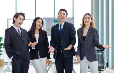 Wall Mural - Millennial Asian successful professional male businessmen and female businesswomen colleagues standing side by side smiling laughing posing gesturing together in company office meeting room.