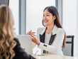 © Bangkok Click Studio - Closeup shot of Millennial Asian beautiful successful professional female businesswoman employee in formal suit sitting smiling talking to colleagues at working desk in company office meeting room