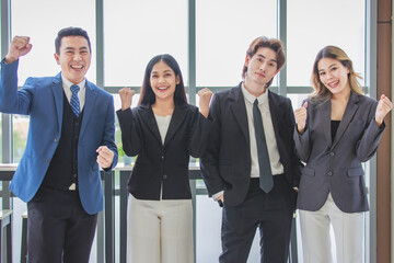 Wall Mural - Millennial Asian successful professional male businessmen and female businesswomen colleagues standing side by side smiling laughing posing gesturing together in company office meeting room.