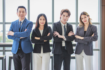 Wall Mural - Millennial Asian successful professional male businessmen and female businesswomen colleagues standing side by side smiling laughing posing gesturing together in company office meeting room.