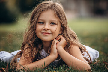 beautiful child girl with white dress, portrait lying on the grass