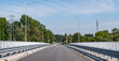 Asfaltowa droga idąca przez most nad rzeką Odrą otoczona barierkami wokół oświetlenie uliczne oraz nieliczne drzewa a na tle błękitne lekko zachmurzone niebo w zachodniej Polsce