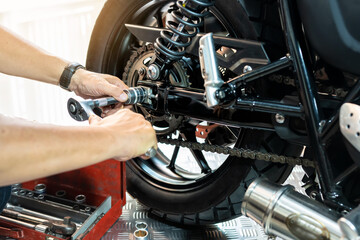 Wall Mural - Mechanic using a wrench and socket to Remove and Replace Rear Motorcycle Wheel, working in garage maintenance, repair motorcycle concept  .selective focus