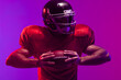 © wavebreak3 - Caucasian male american football player holding ball with neon blue and purple lighting