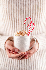 Wall Mural - Girl in knitted wool sweater is holding a mug with hot chocolate with marshmallow.