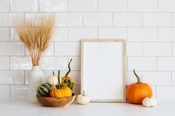 Autumn still life. Photo frame template, decorative pumpkins, vase of dry wheat on white table. Scandinavian room interior.