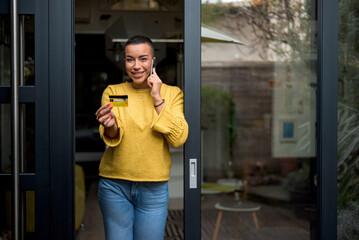 Portrait of attractive young adult woman, talking on the phone holding credit card.