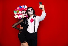 Photo Of Spooky Monster Couple Man Lady Embrace Hold Telephone Make Theme Selfie Picture Wear Short Mini Black Dress Death Costume Roses Headband Suspenders Isolated Red Color Background