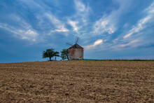 Panorama Of The Landscape On Which Is The Old Mill. In Front Of The Grinder Is A Field And There Are Dramatic Clouds In The Sky At Sunset.