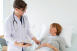 © bung - Professional doctor in the white coat put a stethoscope around neck holding tablet and talked to.elderly woman who lying down on the bed at nursing home. Caregivers provide care medical service.