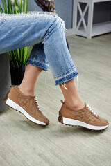 Young woman in blue jeans trying on brown sport shoes in shop, copy space. Woman wearing comfortable stylish sneakers indoors, closeup