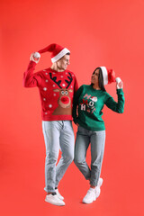 Canvas Print - Beautiful happy couple in Santa hats and Christmas sweaters on red background