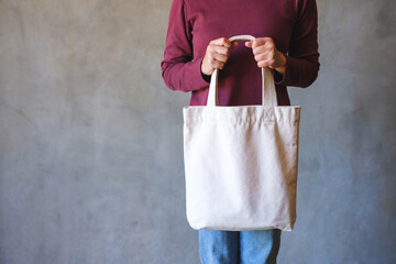 Closeup image of a woman holding and carrying a white fabric tote bag for reusable and environment concept