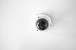 White CCTV with acrylic glass dome cover camera len in the centre hanging from the ceiling. The background is white studio.