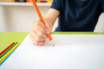 Close up of child hand draws a orange pencil