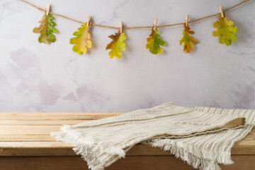 Wall Mural - Empty wooden table with modern tablecloth over autumn leaves garland background. Autumn kitchen mock up for design and product display