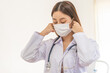 © KMPZZZ - Doctor or physician asian young woman, wearing white coat, stethoscope and medical face mask to protect disease, prevention virus pandemic of covid-19, portrait isolated on background. healthcare.
