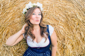 Wall Mural - Beautiful woman in a traditional bavarian dirndl dress posing on a hay bales background. 