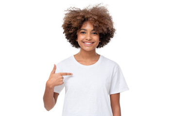 Smiling african girl pointing at her blank white t-shirt with index finger, copy space for your logo, isolated